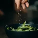Person Pouring Seasoning on Green Beans on Bowl