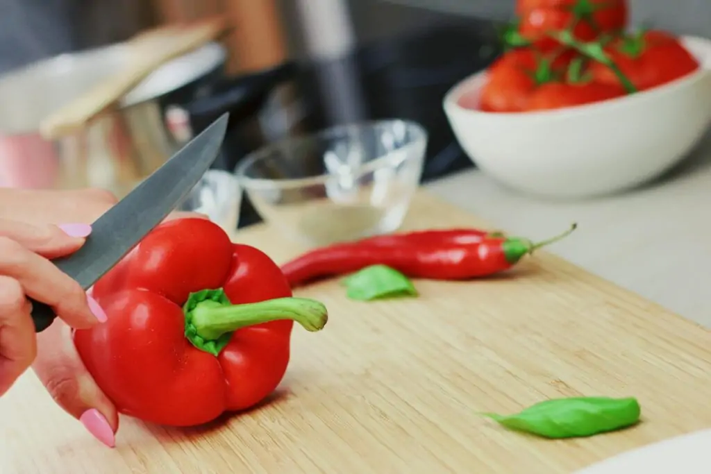 Comment éplucher facilement ses poivrons ? Person Slicing Red Chili Pepper on Brown Wooden Chopping Board
