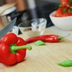 Person Slicing Red Chili Pepper on Brown Wooden Chopping Board