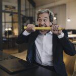 Angry senior businessman with giant pencil at desk in office