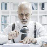 Corporate businessman checking paperwork with a magnifier