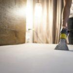 Man cleans the mattress from dust and dirt with washing vacuum cleaner. Bed cleaning process