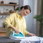 Smiling beautiful housewife ironing the wrinkled shirt