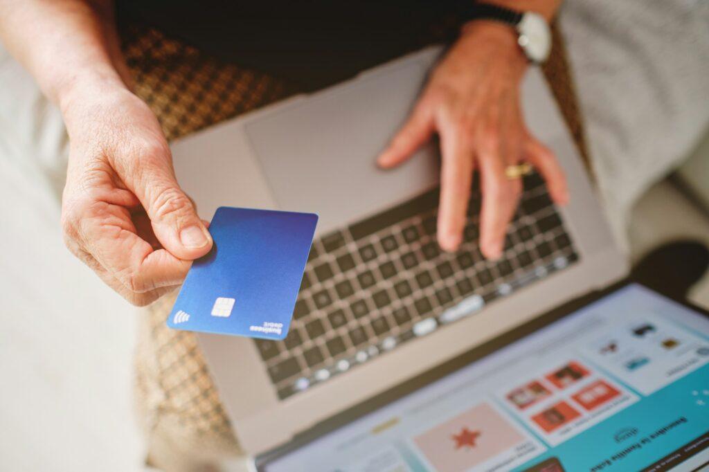 Woman holding a blue credit card with her hand in front of the computer about to pay for a purchase