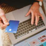 Woman holding a blue credit card with her hand in front of the computer about to pay for a purchase