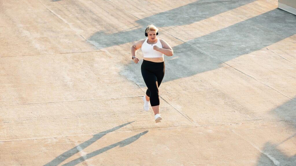 Young curvy female in sportswear jogging on roof.