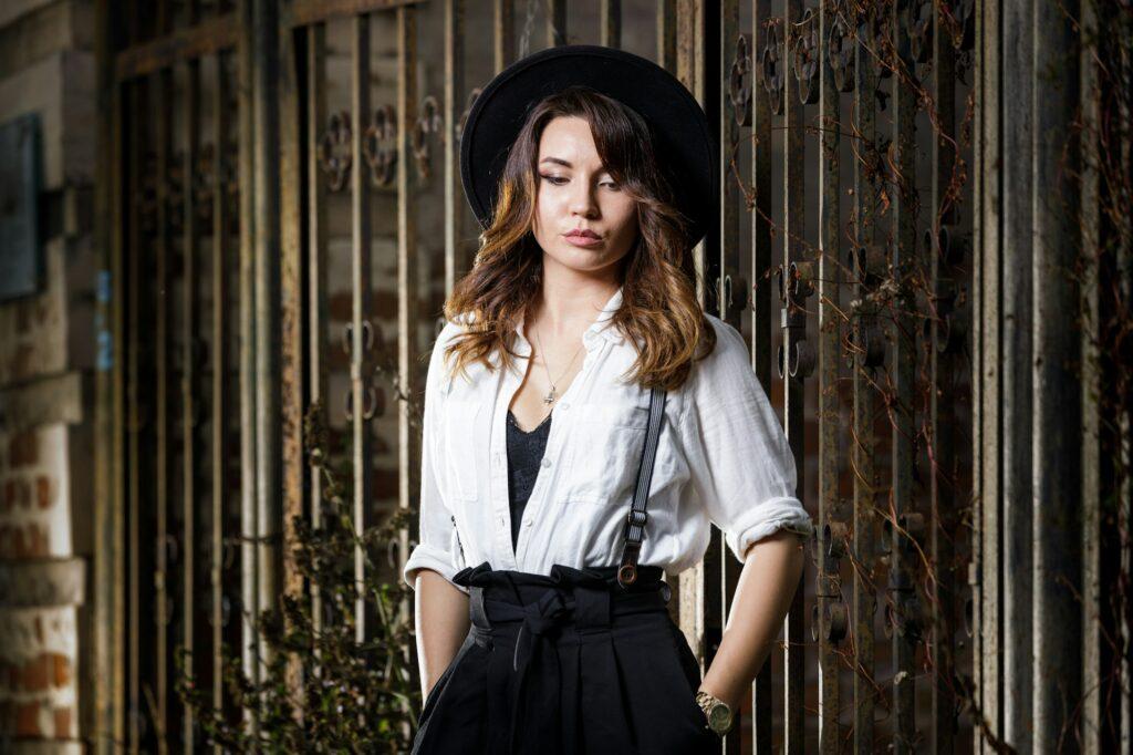 Young woman in white shirt and black hat standing near the gate.