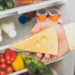 cropped view of man holding cheese near open fridge full of food