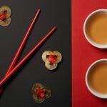 top view of chopsticks with traditional chinese tea and feng shui coins on red and black background