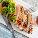 top view of slices of sliced grilled chicken fillet breast on a serving white rectangular plate