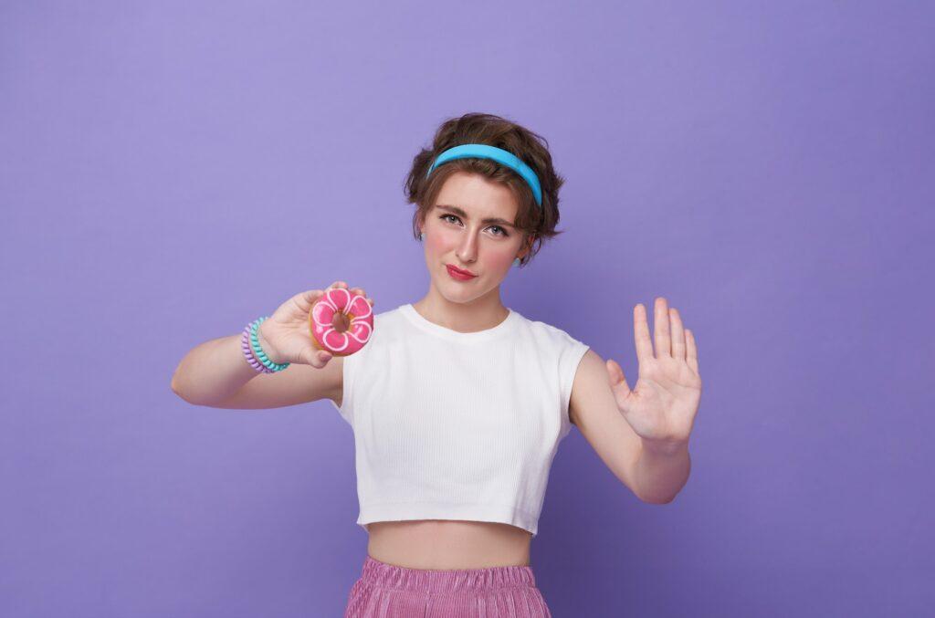 Young sad woman hold eat burger show hand stop gesture say no junk food