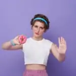 Young sad woman hold eat burger show hand stop gesture say no junk food