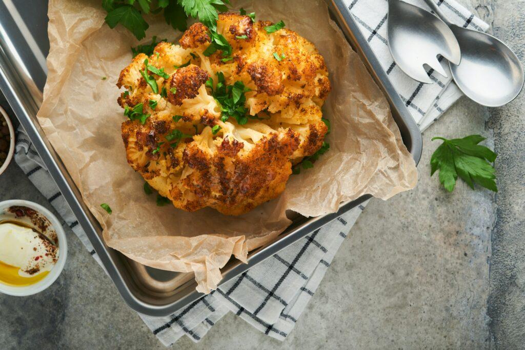 Baked cauliflower. Oven or whole baked cauliflower spices and herbs server on wooden rustic board on