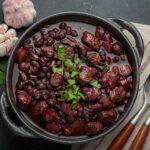 Brazilian feijoada with black beans, sausage and meat in a pot, top view
