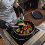 Chef cooking fried cheese with vegetables on frying pan in restaurant kitchen