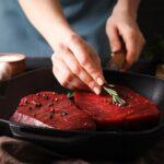 Female chef puts rosemary on raw beef steak, close up