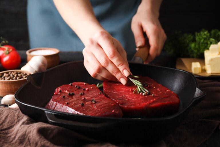 Female chef puts rosemary on raw beef steak, close up