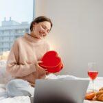 Woman holding gift box using laptop, online dating. Distance relationship, love, Valentine's Day