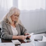 senior woman sitting at table with paperwork and counting money