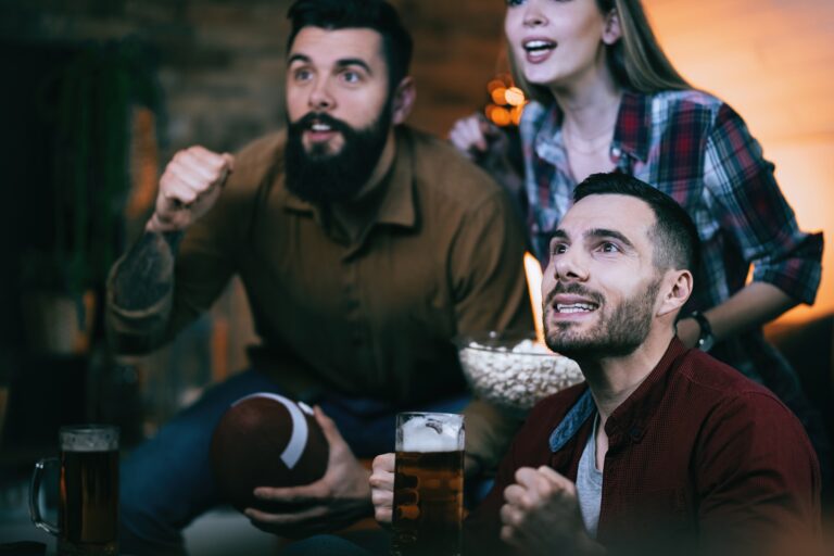 Excited friends watching rugby match on TV at home.