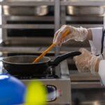 Chef in professional kitchen cooking with frying pan using stovetop.