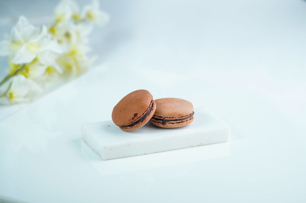 Gros plan sur des macarons au chocolat sur une plaque de marbre avec un doux fond floral, parfait pour les présentations de desserts.