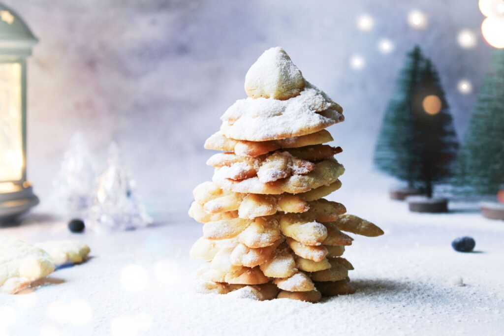 Gros plan sur un sapin de Noël en biscuits empilés avec un saupoudrage de sucre, parfait pour une décoration saisonnière.