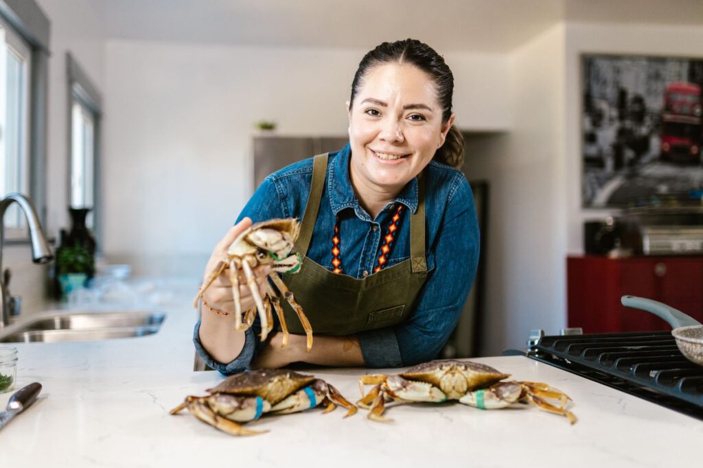 Un chef joyeux présentant des crabes frais sur un plan de travail avec un sourire chaleureux.