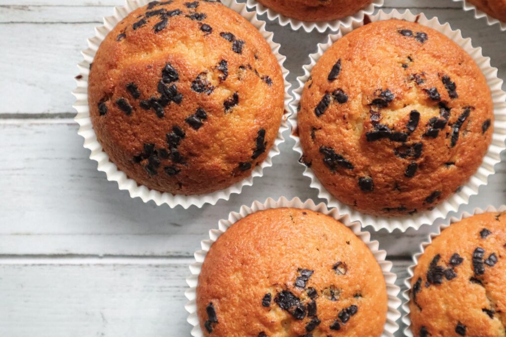 Gros plan de muffins aux pépites de chocolat fraîchement cuits sur une surface en bois blanc, parfaits pour le dessert.