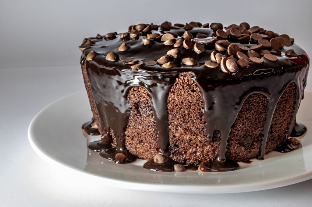 Gros plan d'un gâteau au chocolat garni d'une ganache onctueuse et de pépites de chocolat sur une assiette blanche.