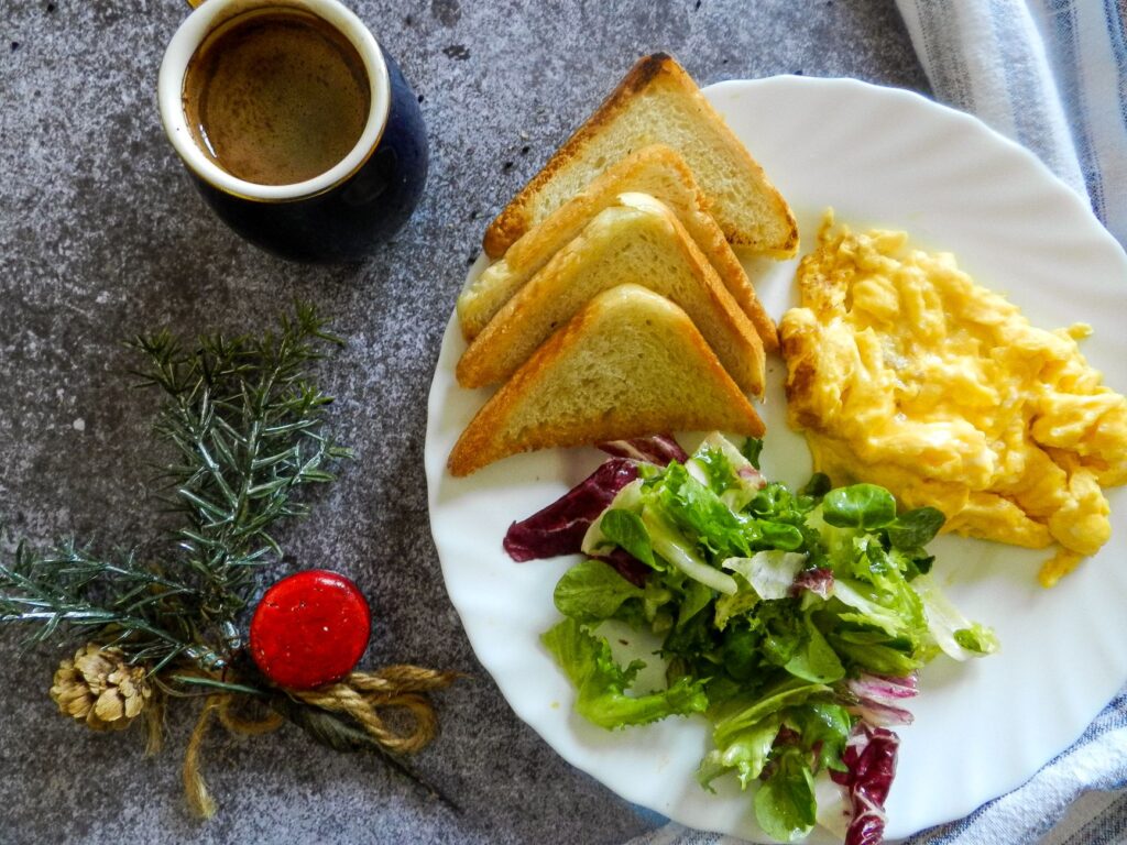 Une assiette de petit-déjeuner avec des oeufs brouillés, des tartines, une salade et du café sur une surface en marbre.