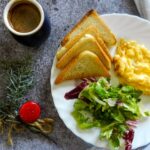 Une assiette de petit-déjeuner avec des oeufs brouillés, des tartines, une salade et du café sur une surface en marbre.