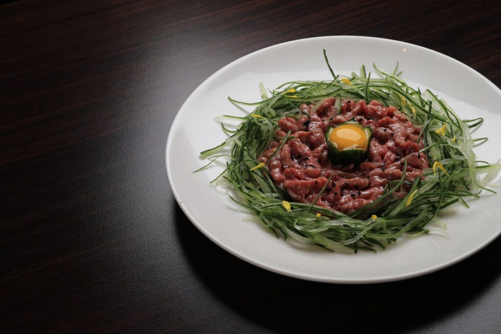 Délicieux tartare de bœuf élégamment présenté avec un jaune d'œuf cru et des légumes frais, parfait pour un restaurant gastronomique.