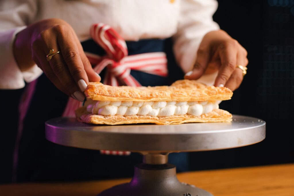 Gros plan sur un chef pâtissier assemblant un délicat dessert mille-feuille avec précision et soin.