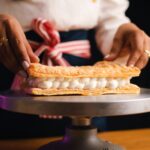 Gros plan sur un chef pâtissier assemblant un délicat dessert mille-feuille avec précision et soin.