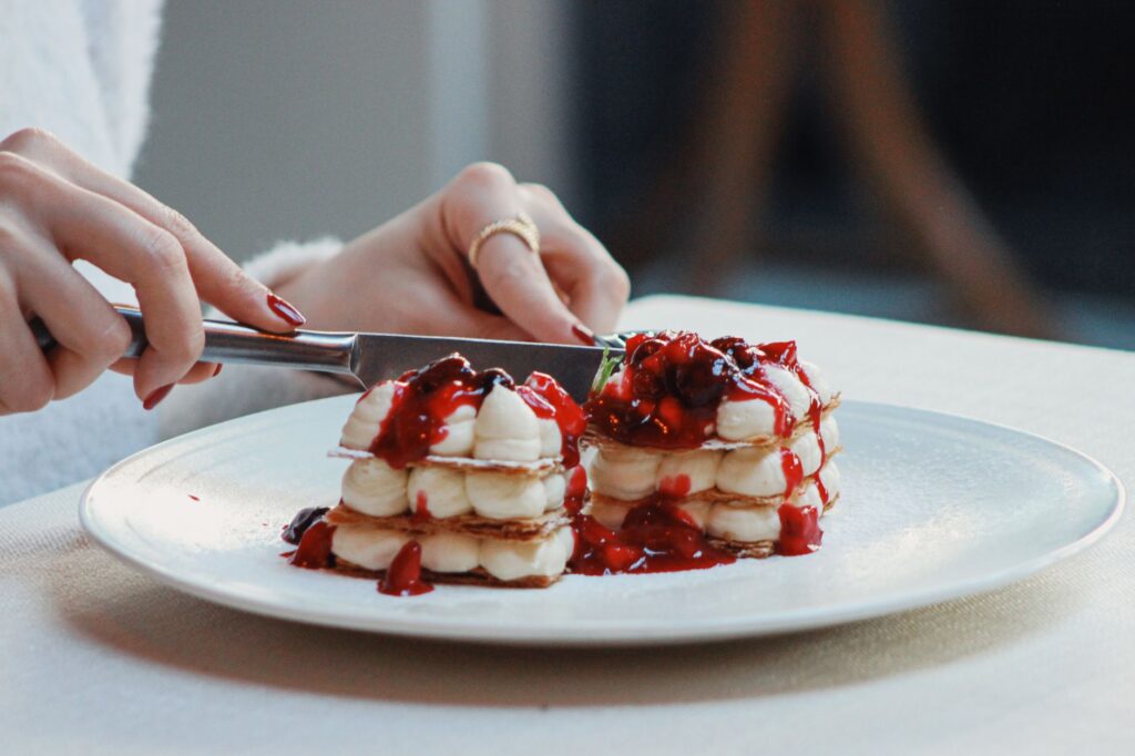 Gros plan sur un délicieux mille-feuille avec des baies en train d'être tranché, créant une scène de dessert tentante.