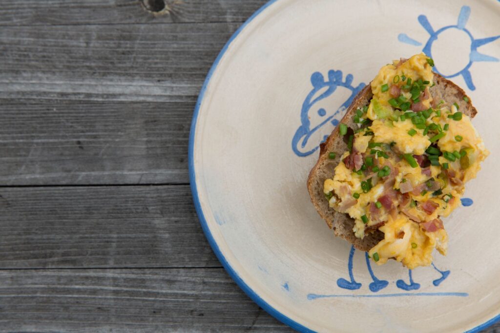 Délicieuses œufs brouillés avec jambon et ciboulette sur toast, servis sur une assiette fantaisiste.