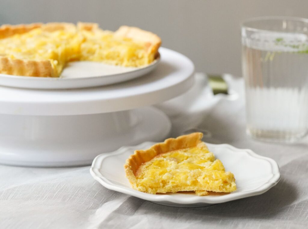 Une délicieuse tarte au citron avec une tranche servie sur une assiette blanche à côté d'un verre d'eau.