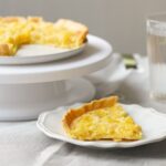 Une délicieuse tarte au citron avec une tranche servie sur une assiette blanche à côté d'un verre d'eau.