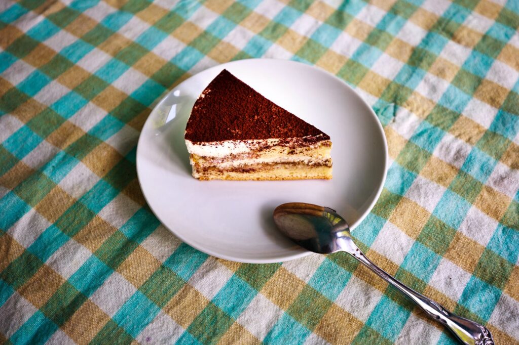 Une part irrésistible de tiramisu dans une assiette blanche avec une cuillère en argent, parfaite pour les amateurs de desserts.