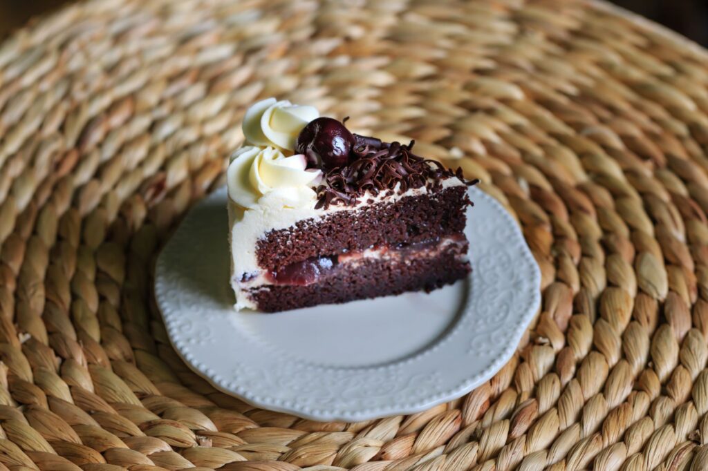 Gros plan d'une tranche de gâteau Forêt-Noire avec de la crème, une cerise et du chocolat sur un fond tissé.