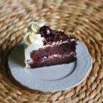 Gros plan d'une tranche de gâteau Forêt-Noire avec de la crème, une cerise et du chocolat sur un fond tissé.