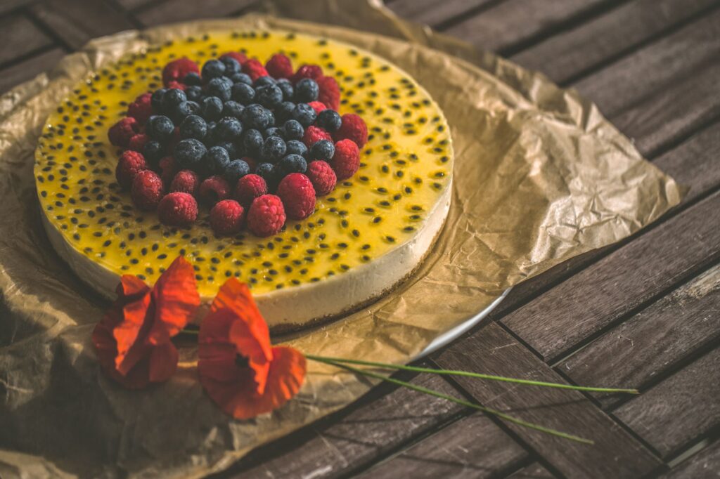Un cheesecake vibrant et frais garni de myrtilles, framboises et fruit de la passion sur une table en bois.