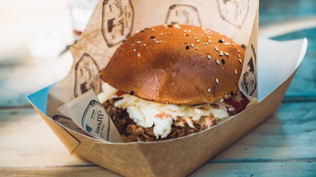 Gros plan sur un burger gourmet avec garnitures dans une boîte à emporter, mettant en avant son apparence délicieuse et attirante.