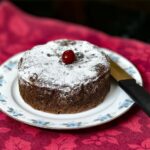 Gâteau au chocolat décadent garni d'une cerise, servi sur une assiette fleurie - parfait pour les festivités.