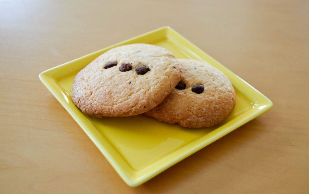 Deux cookies aux pépites de chocolat fraîchement cuits servis sur une assiette jaune.