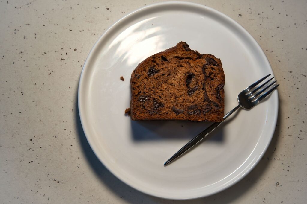 Vue de dessus d'une tranche de gâteau aux pépites de chocolat sur une assiette avec une fourchette, projetant des ombres.