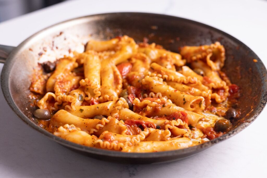 Gros plan de pâtes chaudes cuites dans une riche sauce tomate avec des olives dans une poêle.