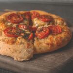 Savoureuse pizza maison garnie de tomates fraîches et de fromage sur une planche en bois.