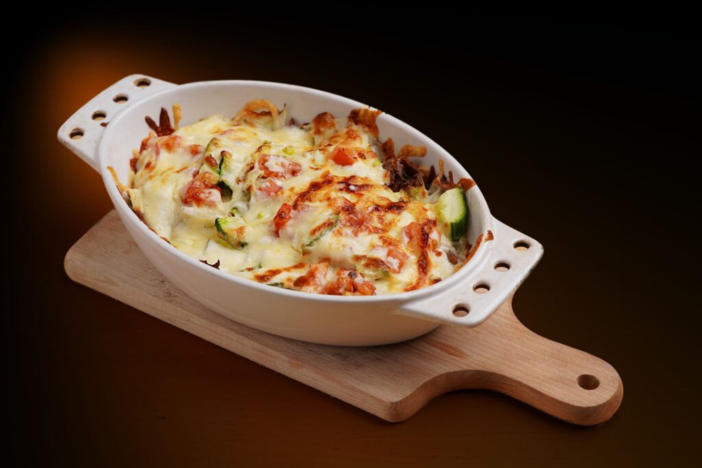 Délicieuse cocotte de légumes cuits au four garnie de fromage dans un plat blanc sur une planche en bois.